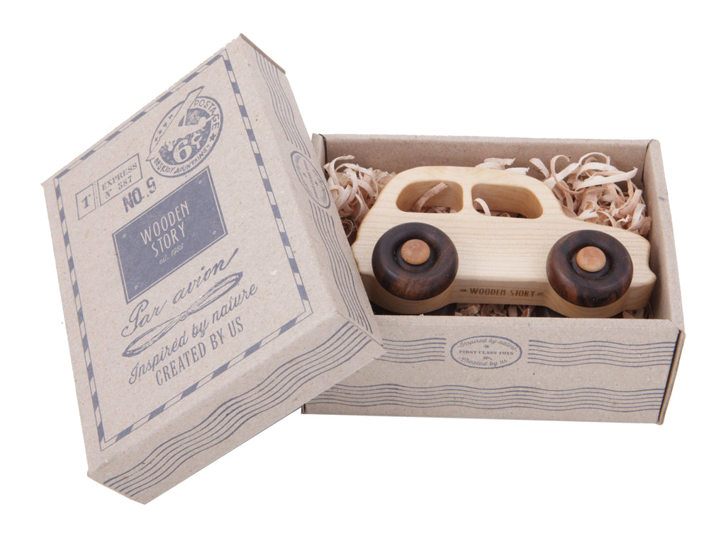 The Little Wooden French Car, a small natural wood baby toy, rests in a gift box with vintage-style designs and shredded paper, visible through the open lid.