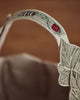 Close-up of the Coral & Tusk Jack-o'-Lantern Basket handle featuring detailed green leaf and red ladybug embroidery, with a green leaf edge design. A softly blurred background highlights this festive basket (ships in one week).