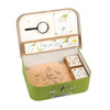 The Moulin Roty Botanist Suitcase is a green case for young botanists, labeled "Le Jardin du Moulin," featuring a magnifying glass, plant cards, envelopes, notebooks, and seed boxes—all organized for botanical adventures.