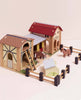 The Wooden Farmyard Stables includes two barn buildings, a fenced area, two toy horses, ladders, and a small trough—all made from FSC-certified wood and displayed on a light surface.