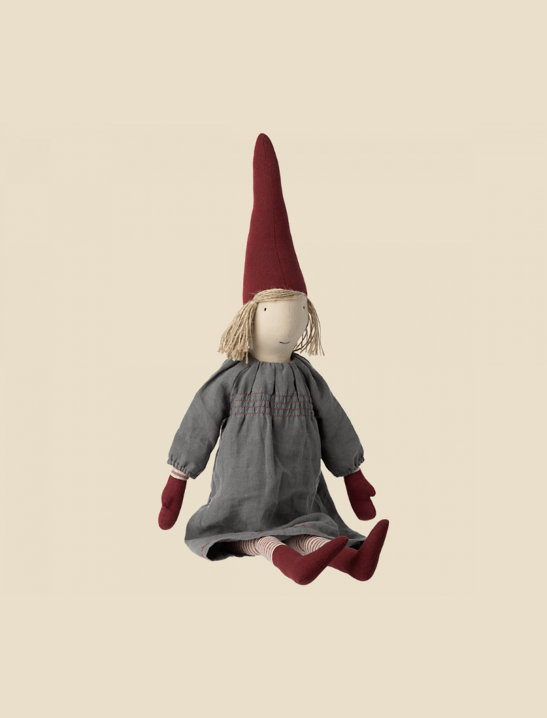 A Maileg Christmas Small Pixy doll with a red pointed hat, a neutral expression, dressed in a grey dress and striped socks, sitting against a cream background.