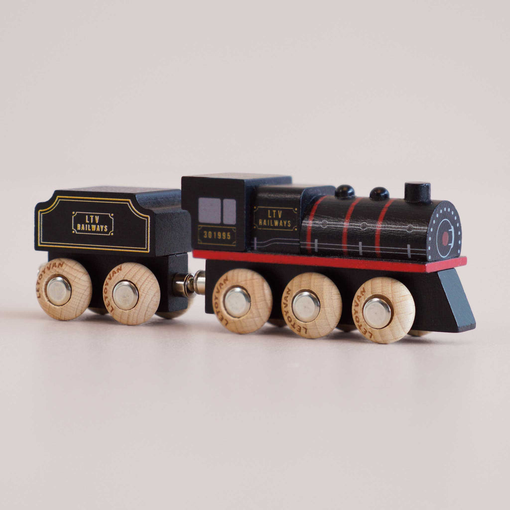 A black wooden toy train labeled “No. 49 GT295 Francis,” handcrafted in England, features red and yellow accents reminiscent of classic steam locomotives. It has six wooden wheels and is displayed on a light background.