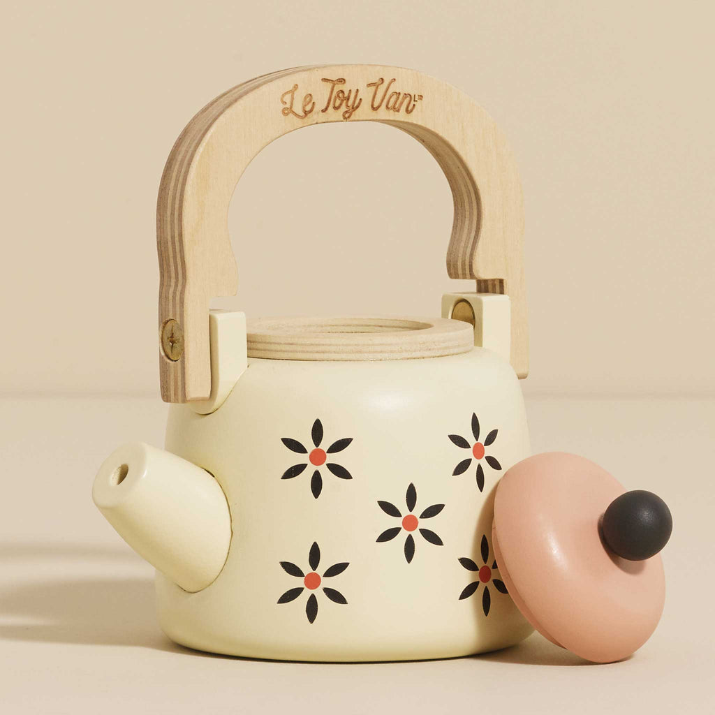 Introducing the Vintage Wooden Role Play Kettle: a delightful toy teapot with a wooden handle crafted from FSC certified wood. It features delicate floral patterns on a beige background, showcasing tiny black and pink flowers against its cream-colored design. The kettle is complemented by its lid, which rests nearby and is topped with a round black knob, adding to its eco-friendly appeal.