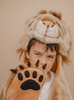 A young child wears the Costume - Lion by Wild & Soft, featuring a fluffy lion suit and a paw-shaped glove, posing in front of a neutral background.