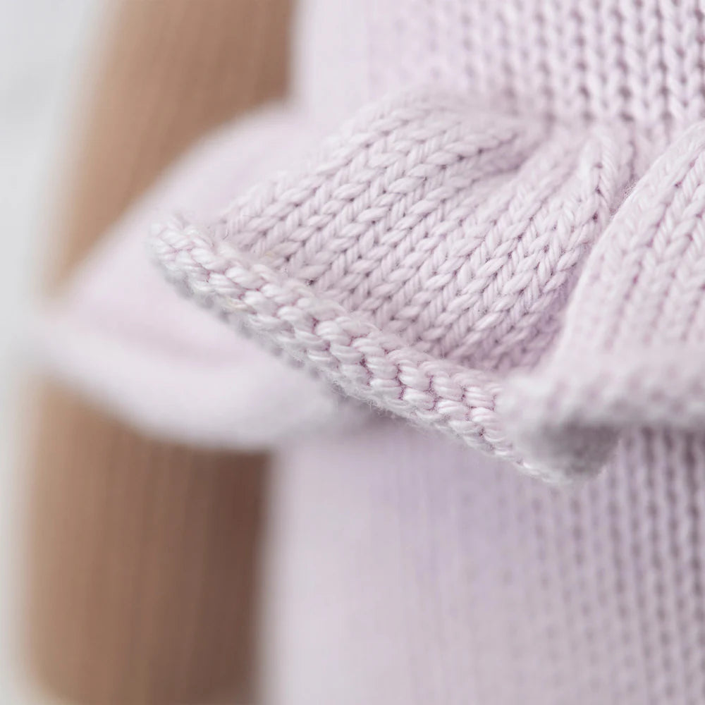 Close-up of Cuddle + Kind Violet the Fawn’s soft, light purple premium cotton knit with ruffled edge, highlighting detailed stitches. A brown texture appears in the background.