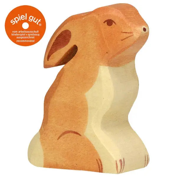 A Holztiger Rabbit, Sitting with a light brown and cream-colored body, sitting upright with its ears pointed back. This handcrafted wood toy features minimalistic detailing and a smooth finish. An orange "spiel gut" recommendation label is visible in the top left corner, proudly stating it's made in Europe.