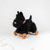 Pull-Along Walter, a plush black dog toy adorned with a red striped collar, sits atop a wooden platform equipped with four wooden wheels and a white pull string—making it an adorable pull-along toy designed to support children's gross motor skill development, all presented against a plain white background.
