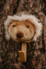 The Coat Hanger - Hedgehog features a plush animal head with a round brown nose, soft beige fur, and a fluffy white mane, displayed against a tree bark background.