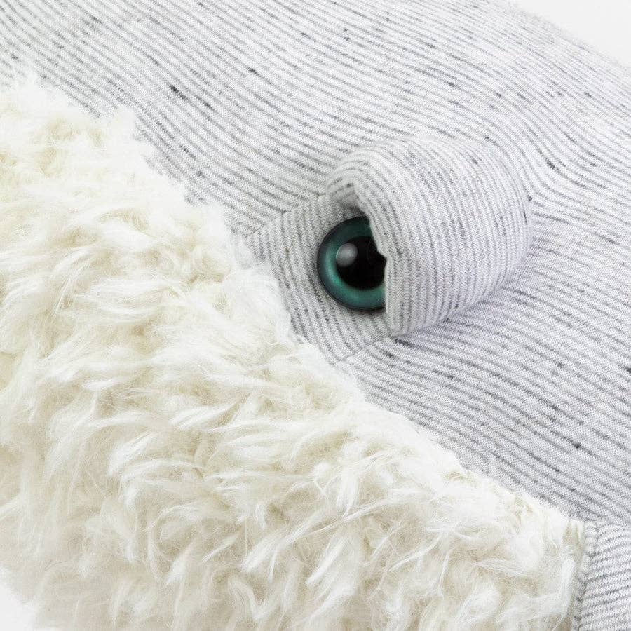 Close-up of a children's stuffed animal resembling a whale, with a grey fabric body and a large blue eye. This soft companion features a white, fluffy texture on its underbelly. The product is called BigStuffed Small Grandpa Whale.