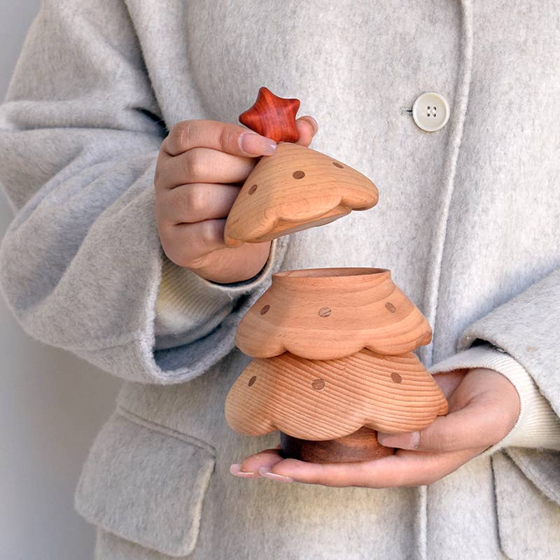A person in a light gray coat lifts the star-topped lid of the Christmas Tree Storage Box, revealing its hollow interior. This festive wooden container features polka dots and is ideal for storing holiday items.