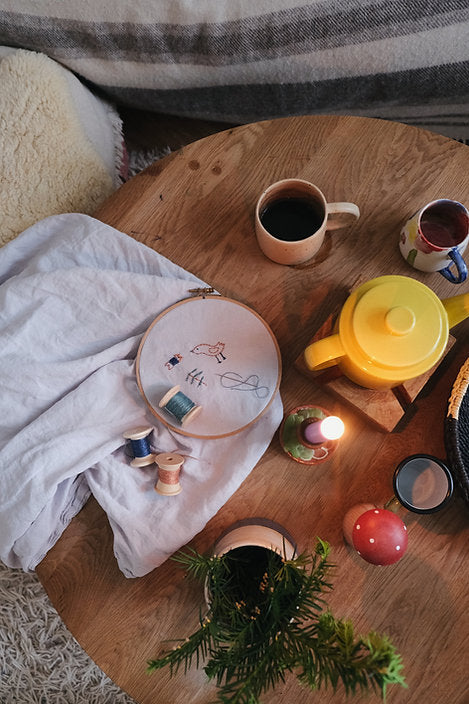 Cozy indoor setting with a limited edition Grapat Advent Calendar (Final Sale), two cups of coffee, a teapot, candles, and apples on a fluffy rug and wooden surface.