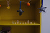 Yellow shelf with small wooden house models from the Grapat Advent Calendar (Final Sale) lined up and colorful hanging decorations including a star, a shark, and an apple.