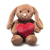 Steiff Hoppie Rabbit – Love is a brown plush bunny with long ears, a pink nose, and black stitched eyes. It sits upright holding a red heart-shaped pillow—a charming gift for Steiff fans. Background is plain white.
