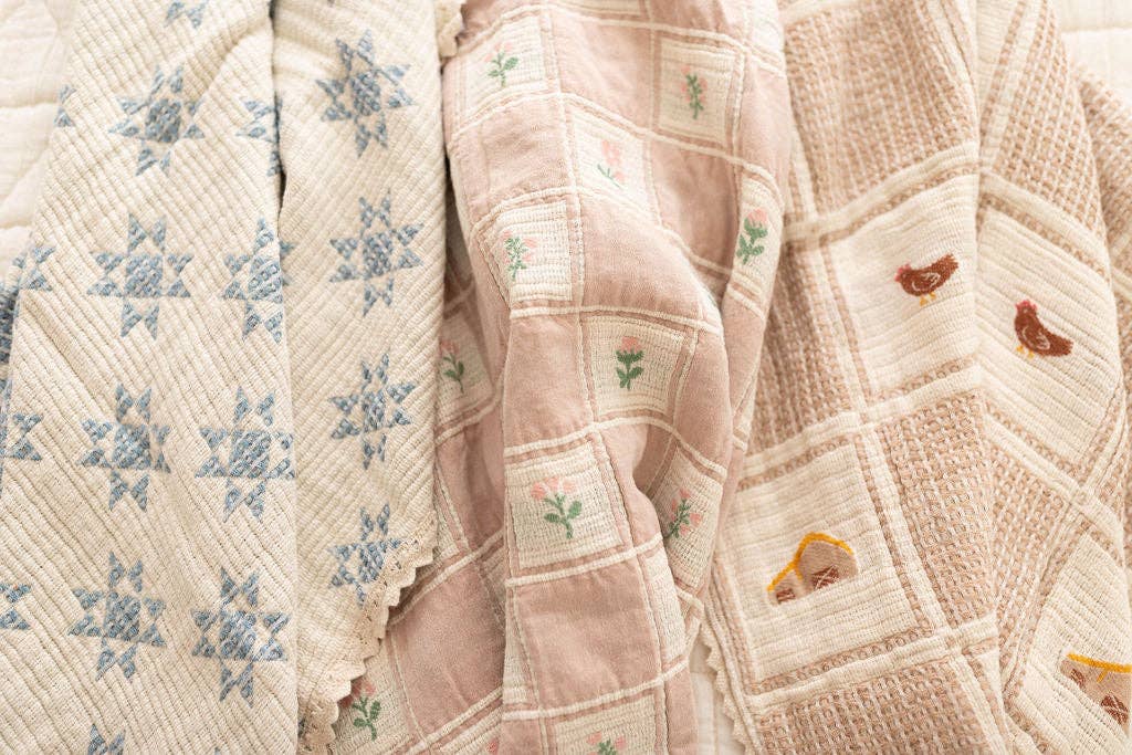The Organic Cotton Baby Blanket - Farm features three vintage-style quilts with soft, muted tones: blue star embroidery on the left, small flowers in the center, and chickens, flowers, and a house embroidered on the right.
