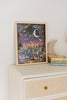 The Mischief Under the Moonlight 300 Piece Puzzle, featuring a whimsical forest scene with animals under a crescent moon, sits on a light dresser beside stacked children’s books and a plush crescent moon toy.