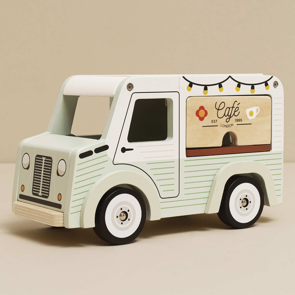 The Mobile Café Van, in pastel green and white FSC-certified wood, features a coffee cup graphic, string lights, and floral accents—ideal for imaginative play on any neutral backdrop.