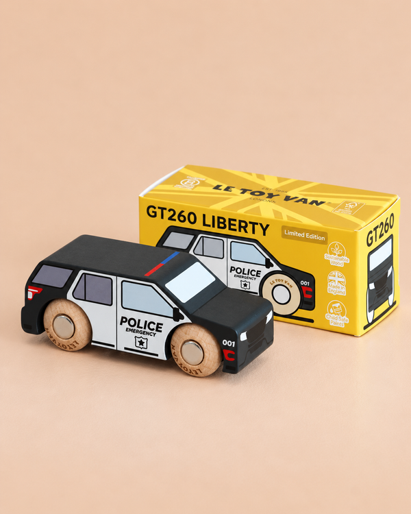 A small black and white wooden police SUV sits on a beige surface next to its yellow box labeled “No. 42 GT260 Liberty | Made in England,” making it a perfect addition to any play collection or a source of imaginative storytelling.