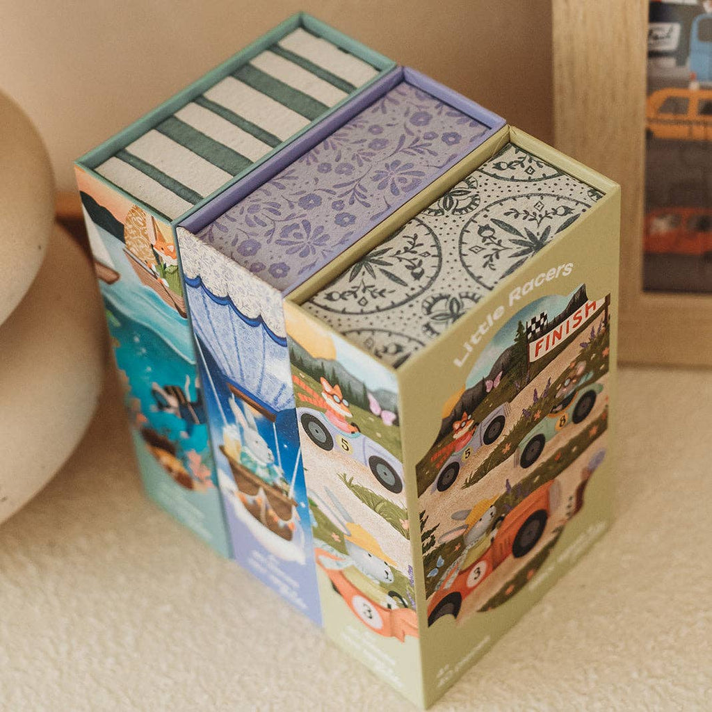 Three colorful rectangular boxes with illustrated designs, including racing cars and playful patterns, are neatly arranged side by side on a light surface near a picture frame. Perfect for young puzzlers, these boxes feature engaging themes such as the Ocean Explorers 40 Piece Mini kids jigsaw puzzle and an exciting ocean adventure scene.