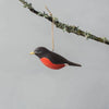 The Hand Carved Hanging Ornament - Robin Bird - 2.5"H features a black head, wings, and bright red underside, suspended by a string from a lichen-covered branch with a plain gray background.