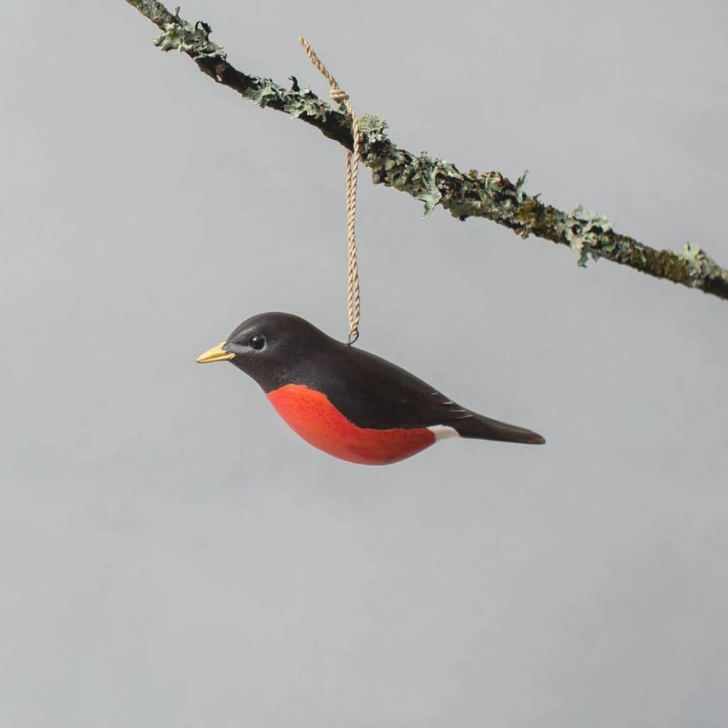 The Hand Carved Hanging Ornament - Robin Bird - 2.5"H features a black head, wings, and bright red underside, suspended by a string from a lichen-covered branch with a plain gray background.