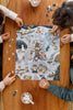 Three children work together to assemble the Midnight Mail 500 Piece Puzzle, featuring whimsical animal characters, on a wooden table as they enjoy mugs filled with marshmallows.