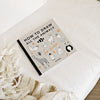 The book "All the Animals: How To Draw Books For Kids" sits on a white surface next to a beige and white blanket, featuring simple animal illustrations on the cover and step-by-step drawing instructions for young artists.