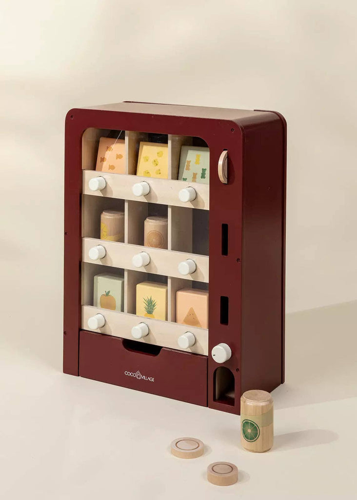 The Wooden Play Vending Machine features a maroon frame, white knobs, and illustrated wooden fruit blocks. It includes two circular tokens and a wooden coin for pretend play and motor skills development.
