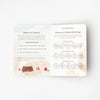An open Slumberkins Fox Kin + Lesson Book On Family Change on a plain background featuring two pages; the left page lists steps for reflection and family change, and the right page shows charts with categories of feelings and supporting icons.