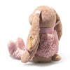 The Steiff Cowgirl Hoppie Rabbit is a plush stuffed bunny with light brown fur, pink ears, boots, and a fluffy vest. Sitting facing away from the camera, it features a long ear with a small yellow tag.