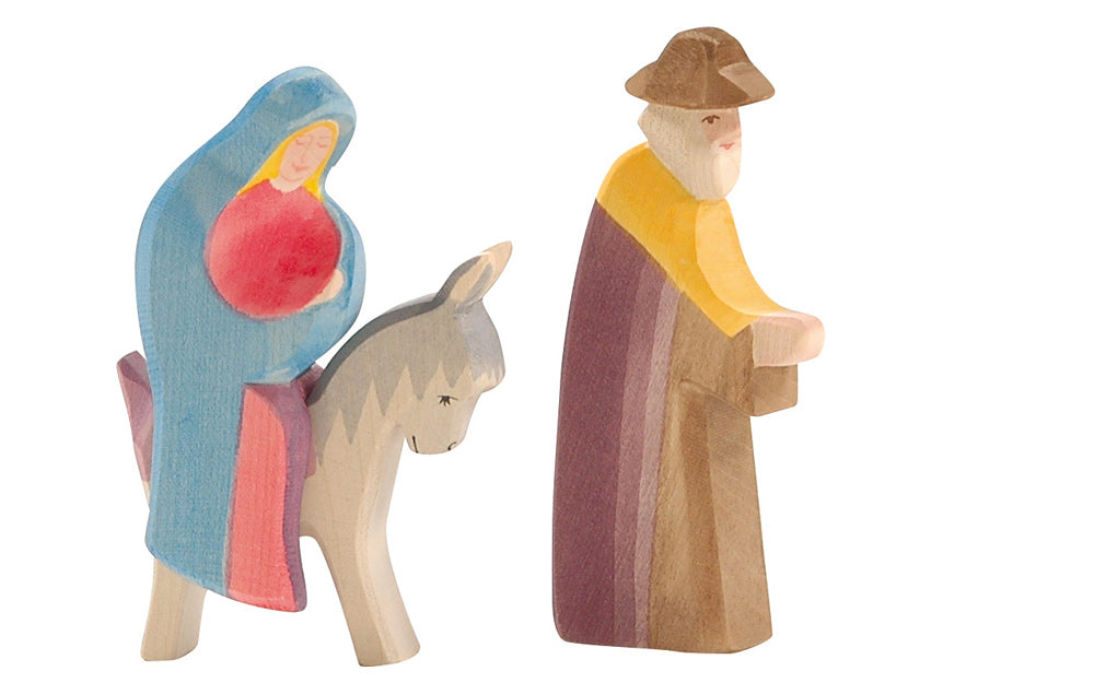 Ostheimer's handcrafted wooden toys beautifully bring the nativity scene to life, showcasing Joseph in a brown cloak and hat walking alongside a figure in blue and red riding a donkey. These figurines capture the essence of imaginative play with charm.