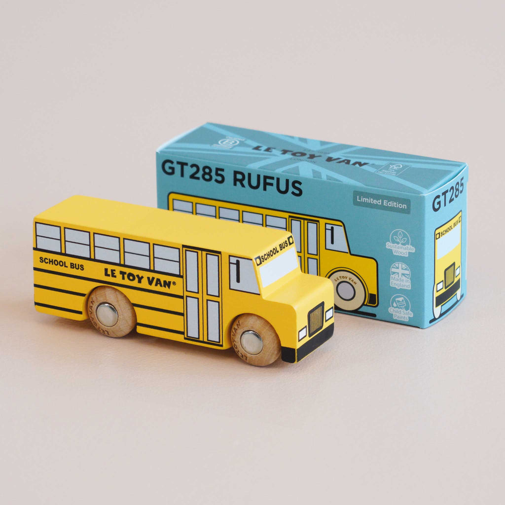 A yellow retro wooden school bus labeled “SCHOOL BUS” and “LE TOY VAN” is displayed next to its blue box, which reads “No. 47 GT285 Rufus | Made in England” and features an illustration of the bus, capturing classic American charm and inviting kids on countless imaginative journeys.