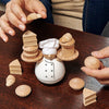 Two hands stack wooden dessert pieces onto the Balance the Baker Stacking Game's chef figurine, balancing treats on his white hat and buttoned coat, as more desserts rest on the table in this delightful balance game.