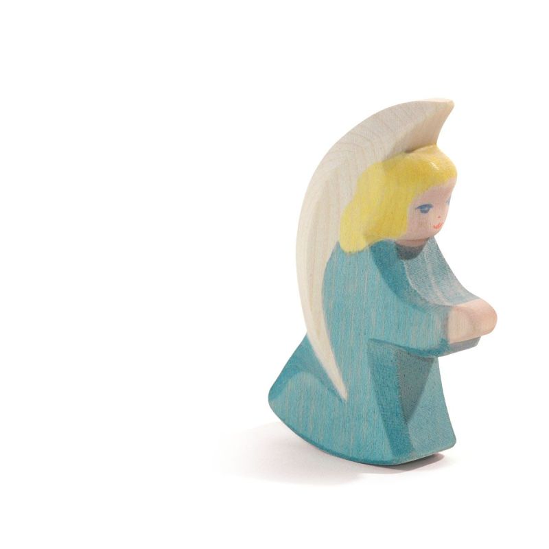 Ostheimer Little Angel - Turquoise: This wooden figurine features an angel with blond hair, donned in a turquoise robe and white wings, kneeling with hands clasped. Handcrafted from sustainably sourced materials, the piece embodies the timeless quality characteristic of Ostheimer wooden toys. The background is plain white.