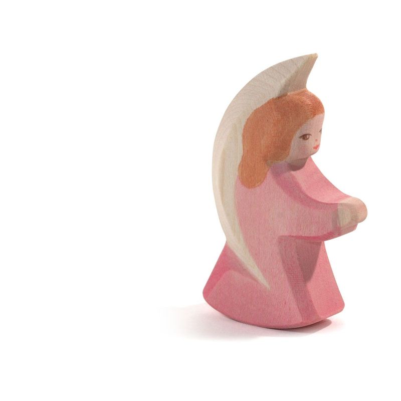 The Ostheimer Little Angel - Pink is a small wooden figurine featuring a kneeling angel with red hair, adorned in a pink dress and white wings. Handcrafted from sustainably sourced materials, this enchanting piece perfectly captures the essence of Ostheimer toys. The figure is set against a plain white background.