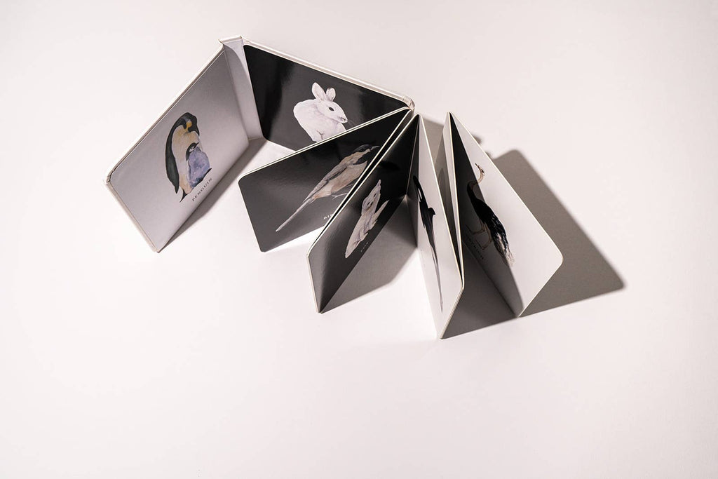 The Black and White Contrast Book for Baby is a compact, accordion-style book open on a white surface with dramatic shadows, featuring high-contrast black-and-white images of animals like a bird, mouse, and rabbit—ideal for supporting visual development in little ones.