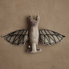 The Coral & Tusk Bat Surprise Doll, featuring fabric bat wings, embroidered accents, and a neutral palette, hangs against a textured beige wall.