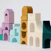 Grimm's Small Building Set - Floors features colorful wooden blocks in architecturally inspired shapes—arches, rectangles, and cylinders—in shades of yellow, purple, blue, white, and green, stacked to resemble a vibrant cityscape.