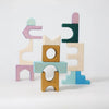 Pastel blue, yellow, green, purple, and cream blocks from Grimm's Small Building Set - Floors are stacked in whimsical, abstract shapes. Their unique architectural forms stand out against a plain white background.