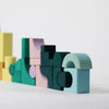 The Grimm's Small Building Block Set - Movement features colorful wooden blocks in shapes like arches, rectangles, and semi-circles, arranged as an abstract construction on a white surface with a plain background.