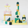 Grimm's Small Building Block Set - Movement features colorful wooden blocks in green, yellow, natural wood, white, and pastel tones. Abstract shapes stack on a pale yellow base to create imaginative structures from the TINY ART COLLECTION.