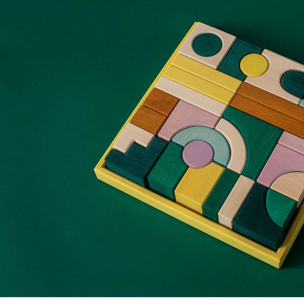 The Grimm's Small Building Block Set - Movement features a yellow tray with colorful wooden blocks in pastel shades and various shapes, ideal for creative building, displayed neatly on a dark green background.