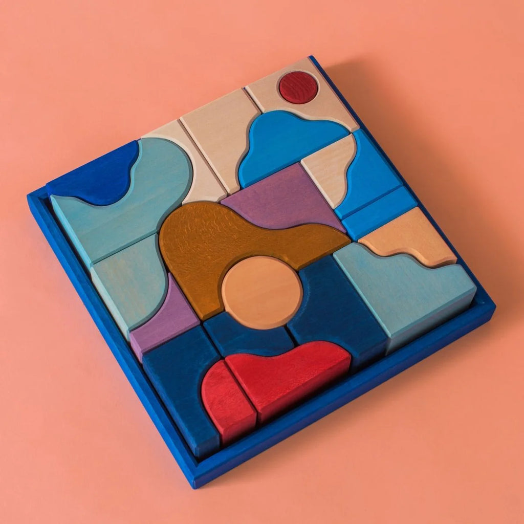 Grimm's Small Building Block Set - Wave features colorful wooden puzzle pieces in various shapes arranged in a blue square frame on a peach background, perfect for inspiring creative play and imaginative building.