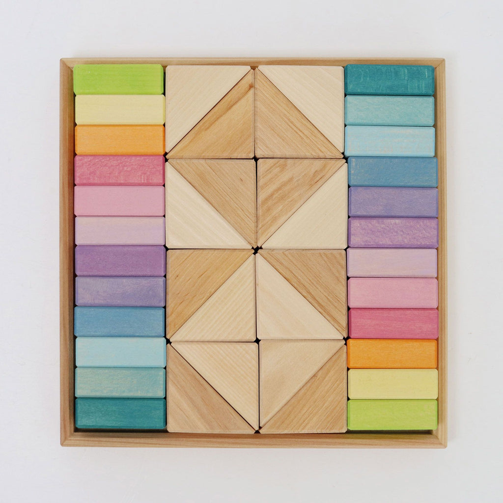 The Pastel Duo Block Set is a neatly organized wooden block collection featuring an assortment of geometric shapes. It includes colored rectangular and triangular pieces arranged symmetrically within a square wooden frame. The blocks come in hues such as green, yellow, blue, purple, pink, and natural wood.