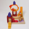 Grimm’s Building World - Desert Sand blocks and three small peg dolls are arranged on a wooden tray to create a miniature playground for imaginative free building.