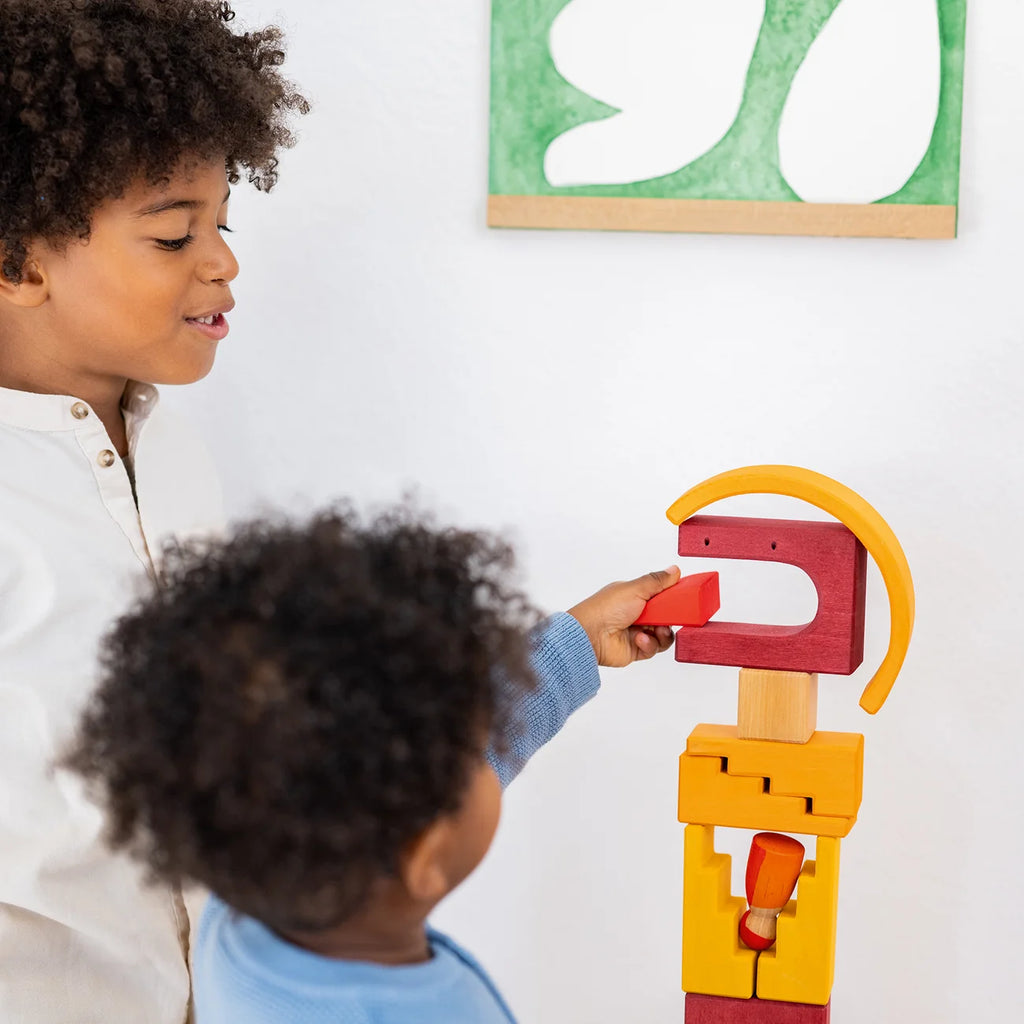 Two children engage in imaginative free building as they stack the colorful, uniquely shaped wooden blocks of a Grimm’s Building World - Desert Sand set into a tower.