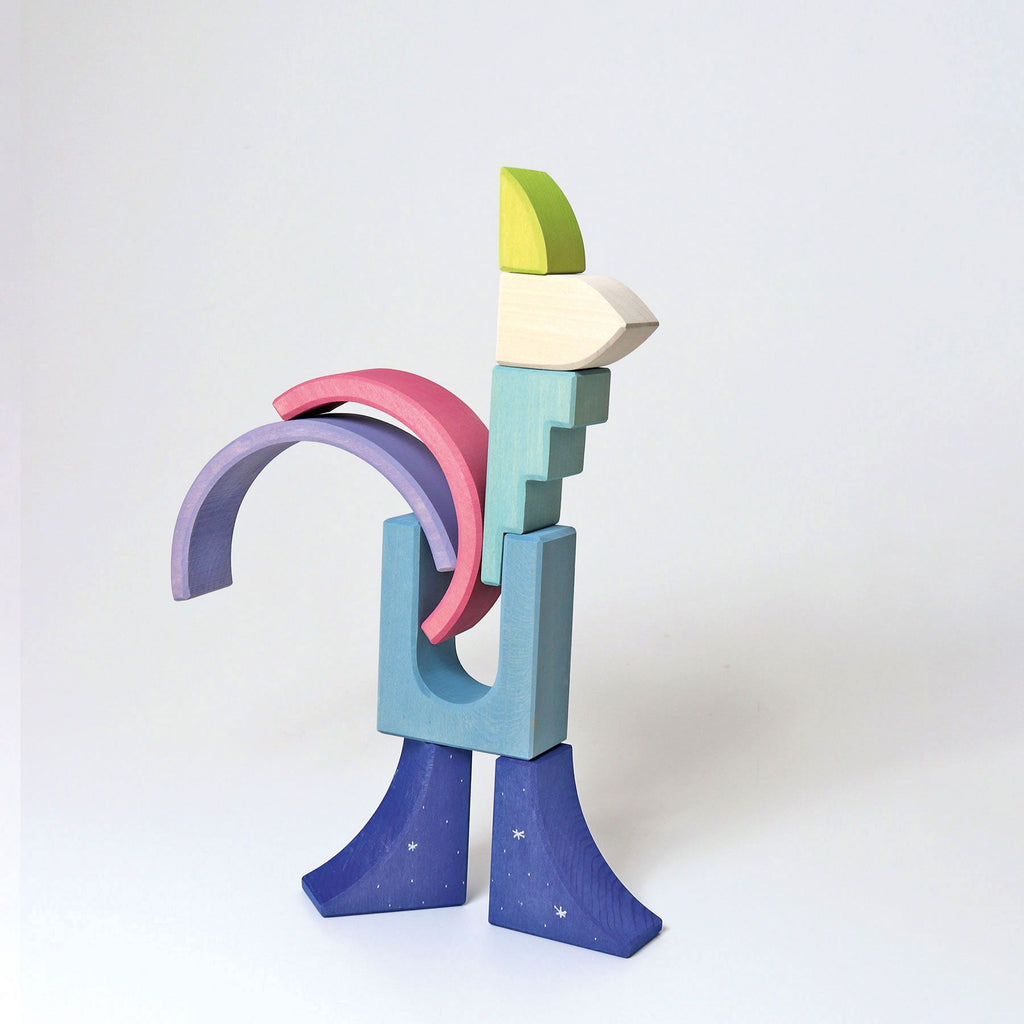 A colorful, abstract structure made of variously shaped wooden blocks is arranged to resemble a quirky, modern sculpture. The blocks include arches, rectangles, and other geometric shapes in pastel colors like blue, pink, purple, yellow, and green—perfect for small Grimm's Building World Polar Light Block Set.