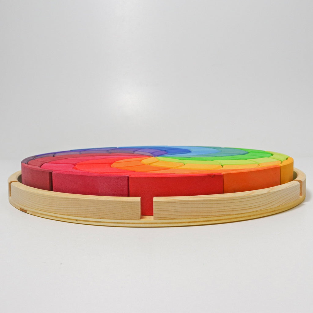 A Grimm's Wooden Color Spiral Block Set in the shape of a circle, composed of varied segments painted in a gradient from red to blue. The puzzle is set on a plain background with a wooden frame encircling it, perfect for young builders to develop their fine motor skills and spatial thinking skills.