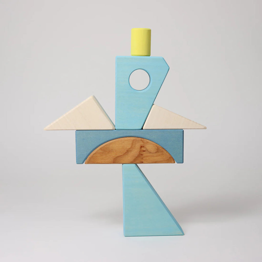 The Grimm's Building Set - Blue includes wooden blocks and blue pieces arranged to resemble a bird with a yellow cylinder head, white triangle wings, and a blue and natural wood body—perfect for inspiring creativity in toddlers.
