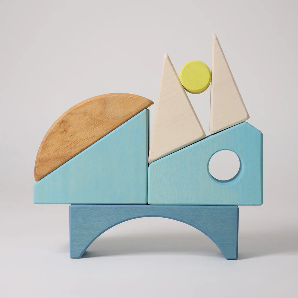 Grimm's Building Set - Blue features pastel wooden blocks in blue, beige, yellow, and natural wood tones, stacked to create a playful animal or abstract figure—an ideal toddler toy shown against a plain background.