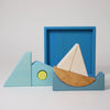 Grimm's Building Set - Blue features colorful wooden blocks arranged as a sailboat and geometric shapes in blue, white, yellow, and natural tones—a vibrant toddler toy displayed on a plain white background.